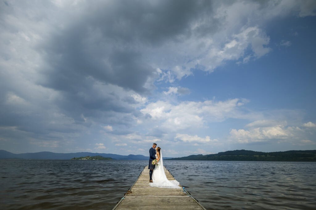 Bride and groom stand on the jetty of the cruin, right in the middle of Loch Lomond