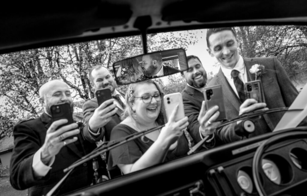 couple kiss in car as guests take their own pictures